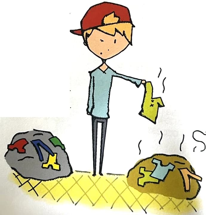 A boy holds up a smelly shirt between a clean pile and a dirty pile of laundry.